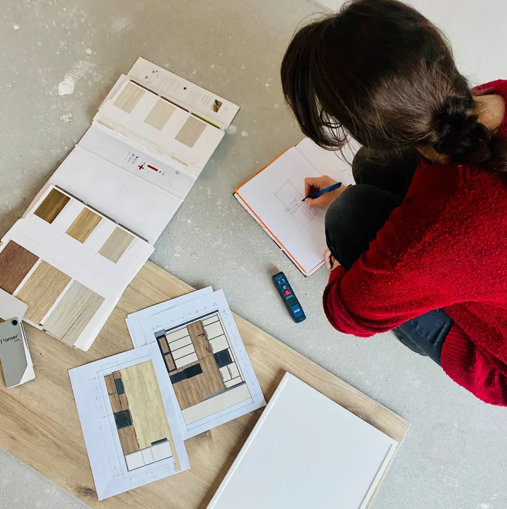 A designer sketching at a desk covered with wood and tile samples, seen from above