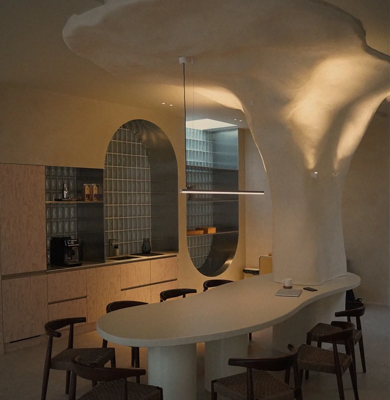 A long organic work table that grows out of the studio's structural column, with the kitchen installation behind