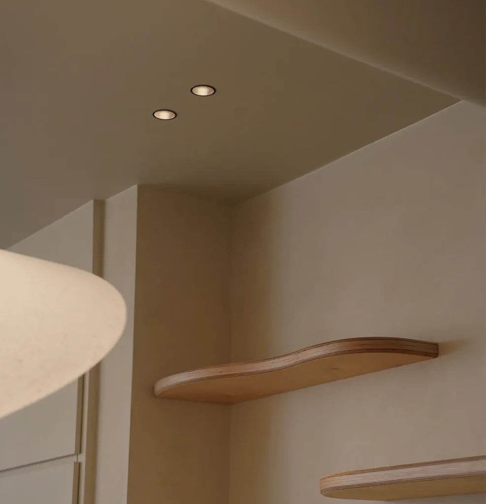 Curved oak shelves on a plaster wall beside a sculpted white form