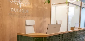 Curved reception desk clad in green artisan tiles before an oak-veneered wall with the clinic's sign