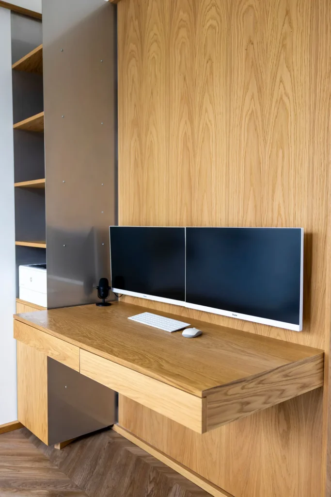 A floating oak desk with two monitors set into an oak-veneered wall
