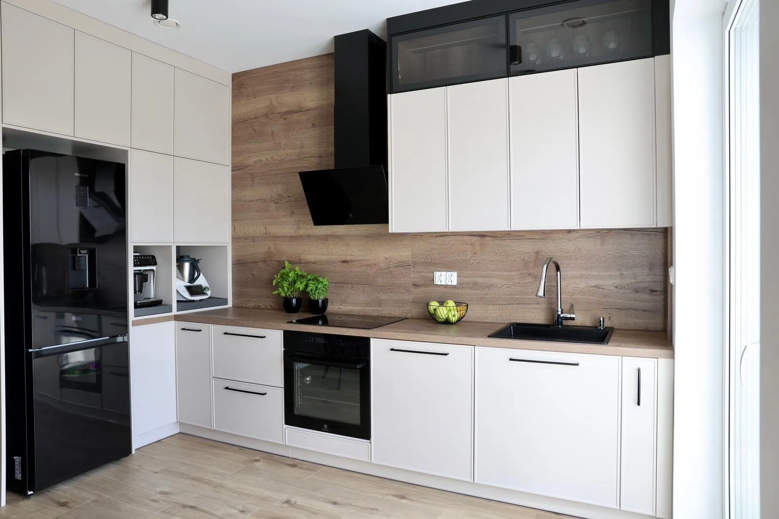 A white handleless kitchen with a full-height oak splashback, black hood and a tall black fridge