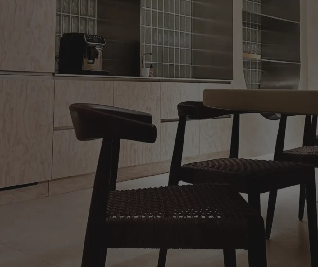 Dark wooden dining chairs with woven seats in front of a plywood kitchen with an arched glass-block niche