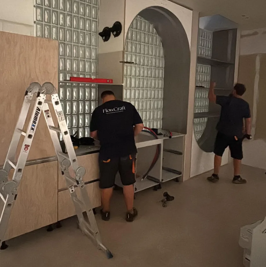 Two FlowCraft fitters assembling cabinetry and an arched glass-block wall on site
